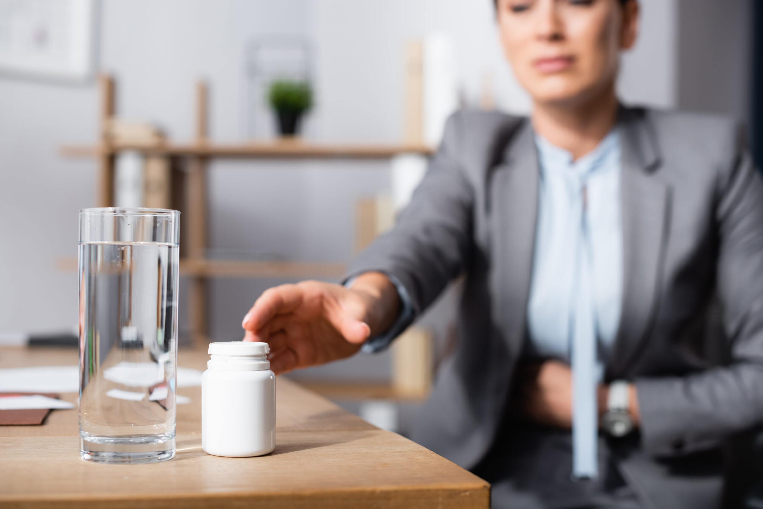Image of a person at work reaching for a glass of water and a bottle of pills.